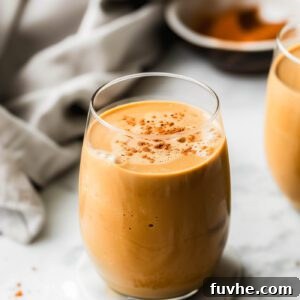 A creamy sweet potato smoothie in a glass sprinkled with cinnamon with a dish cloth laid out behind it.