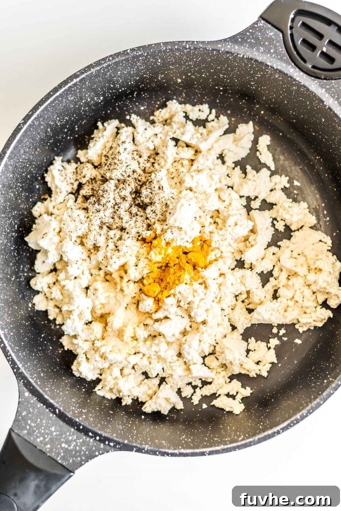 Plant-Powered Breakfast Tacos 3 Crumbled firm tofu coated with turmeric, garlic powder, salt, and pepper in a skillet, ready to be cooked into a delicious plant-based scramble.