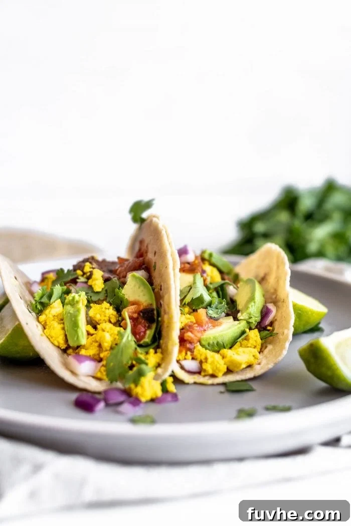 Plant-Powered Breakfast Tacos 5 Two generously stuffed vegan breakfast tacos featuring fluffy tofu scramble, creamy avocado, and savory refried beans, presented on a plate.