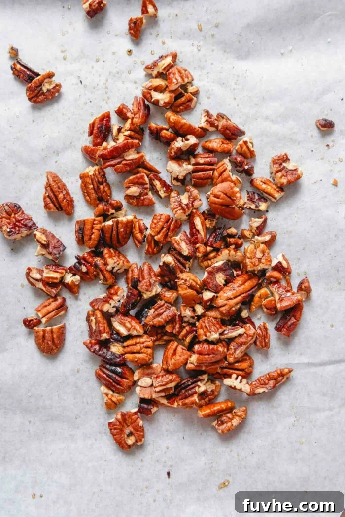 Candied chopped pecans spread out on a baking sheet lined with parchment paper to cool and crisp up.