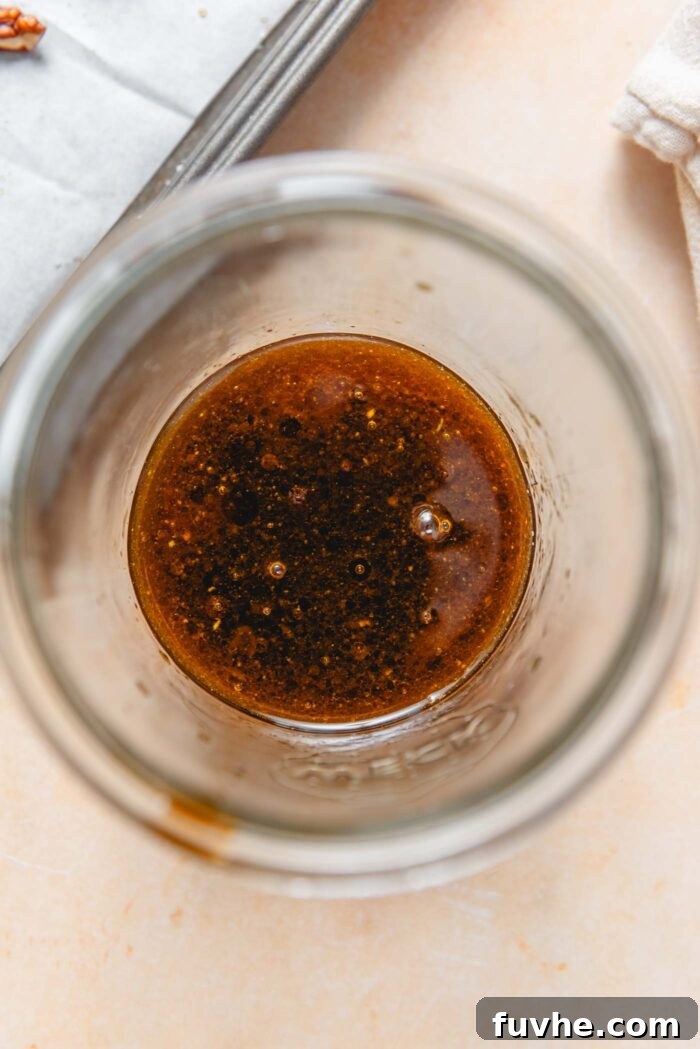 Homemade balsamic salad dressing being whisked in a clear glass jar, showing its rich color and smooth texture.