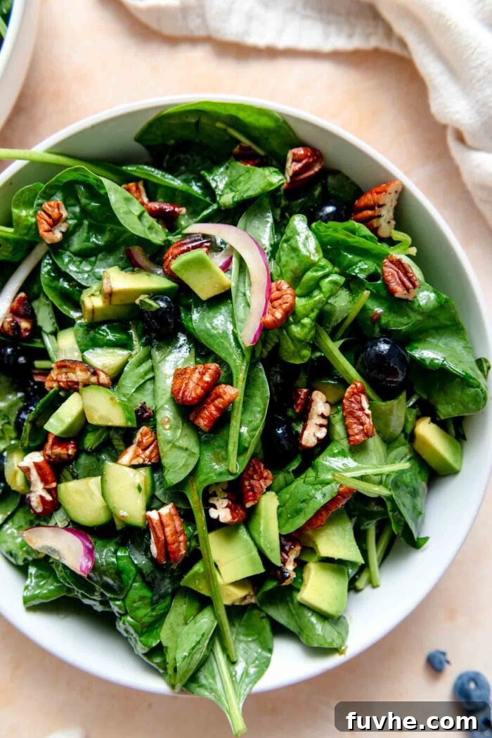 A beautifully plated bowl of blueberry spinach salad, garnished with a generous sprinkle of candied pecans and perfectly diced avocado, ready to be enjoyed.