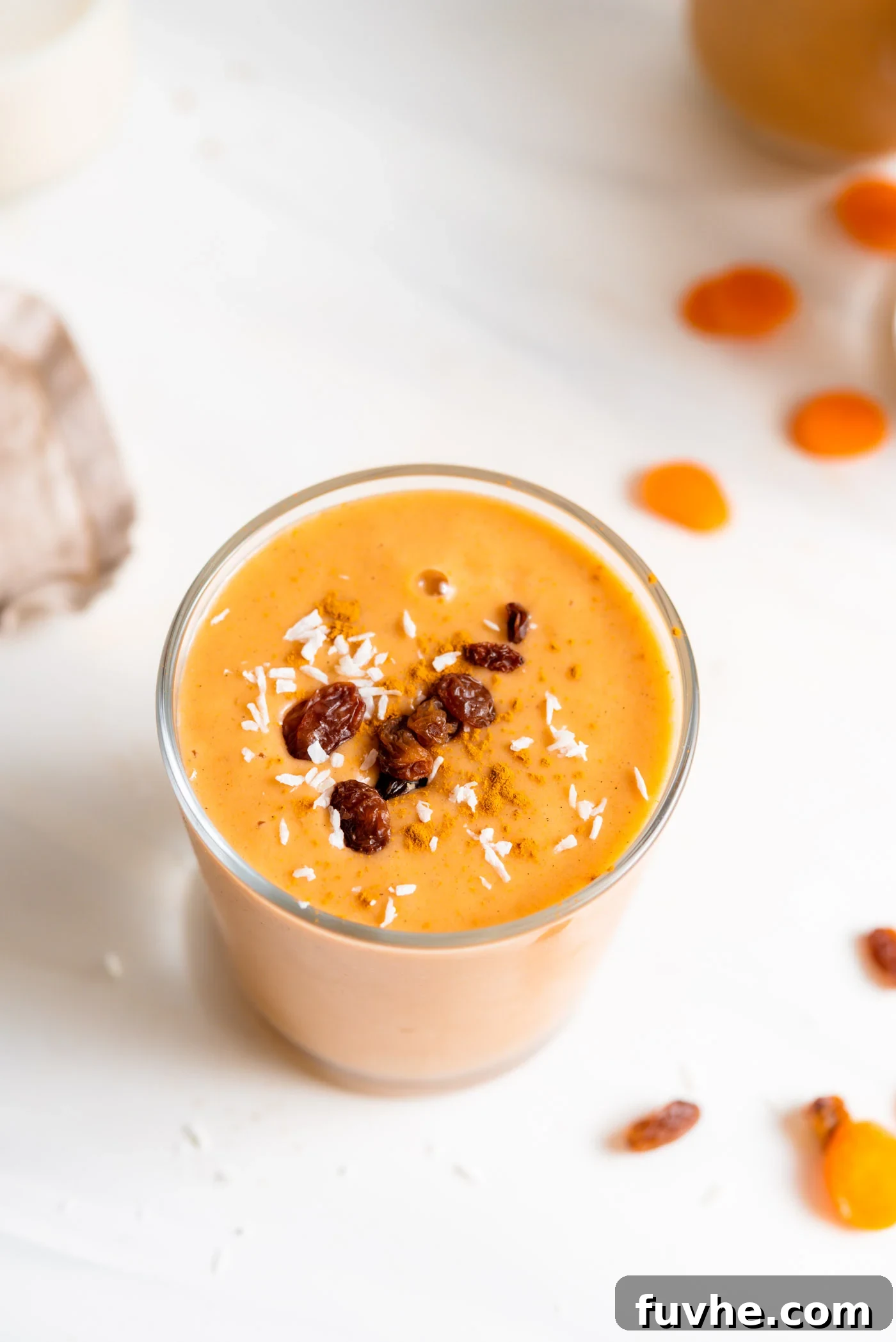 Creamy carrot smoothie in a glass topped with a few raisins.