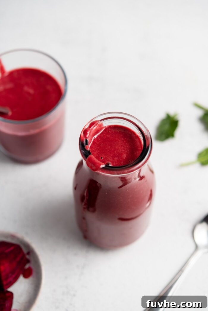 Beet orange protein smoothie served in a glass jar, with a smaller glass and fresh beet slices in the background.