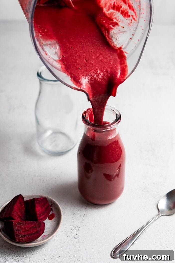 Pouring a vibrant beet orange smoothie from a blender into a clear jar.