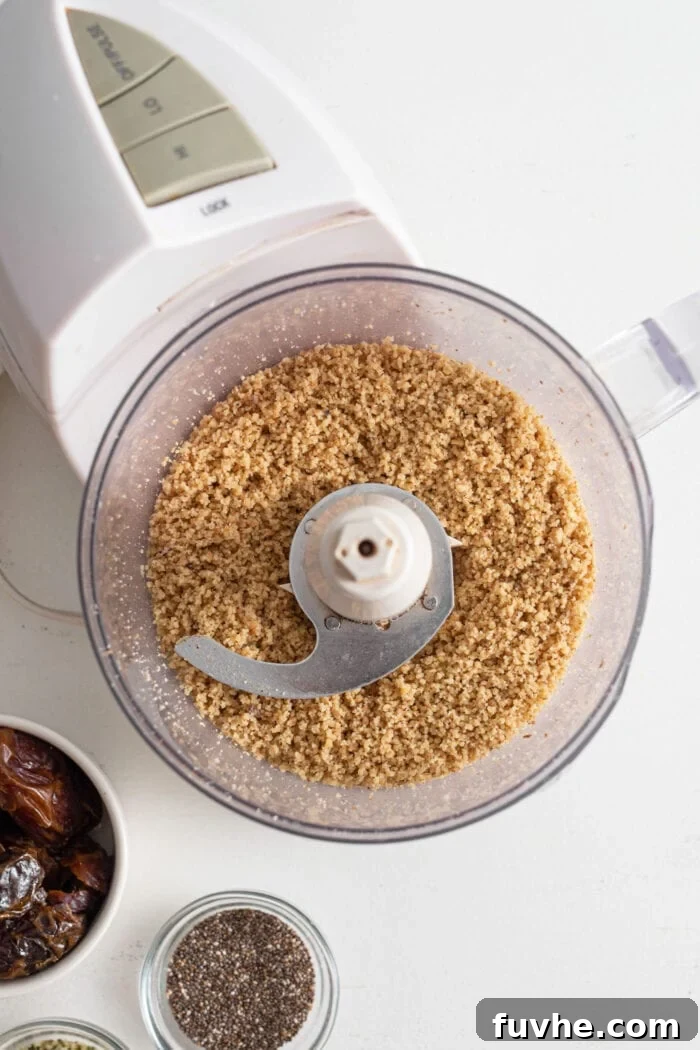 Blended walnuts in a food processor. A small glass bowl of chia seeds and dates is beside the food processor.