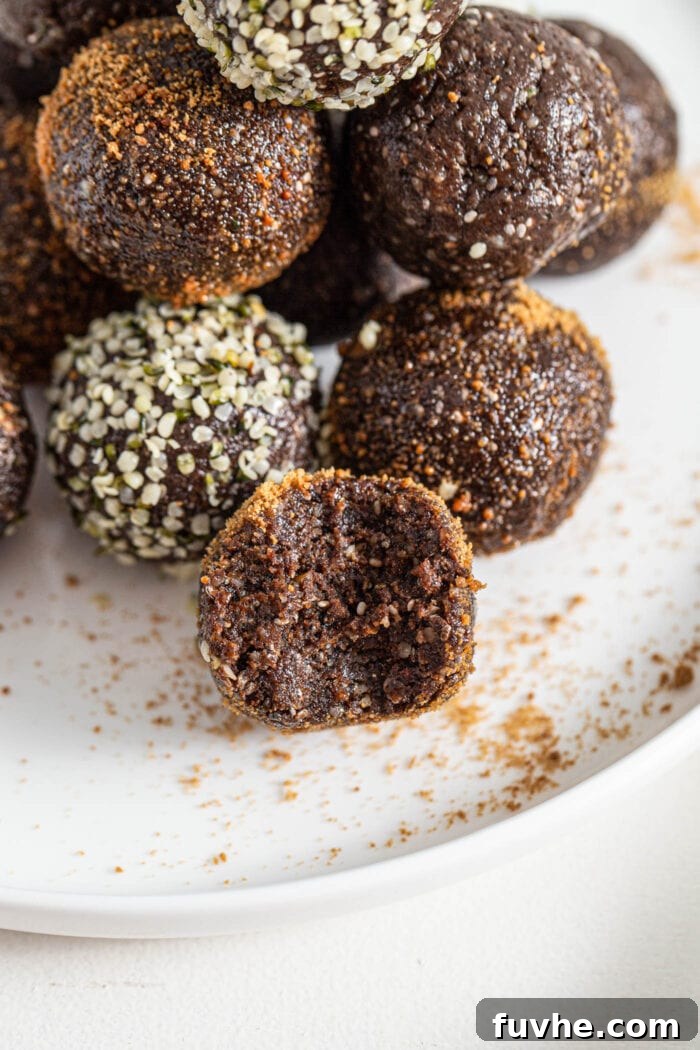 Close up of a superfood chocolate energy ball coated in coconut sugar with a bite taken out of it on a plate. There are more chocolate energy balls on plate in background, some are coated in hemp seeds.