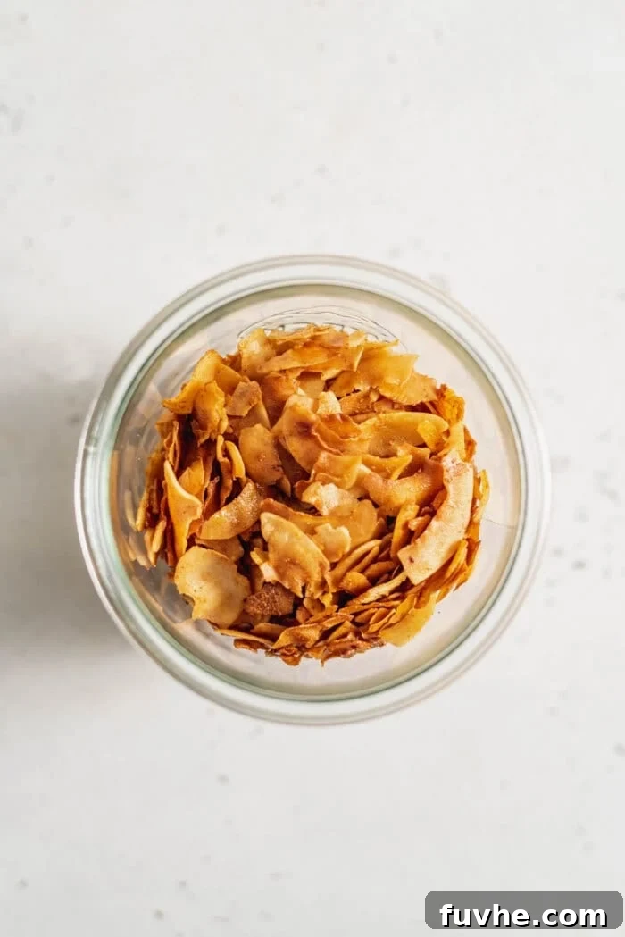 Smoky Coconut Crisps 2 Glass jar of vegan coconut bacon sitting on a white surface.