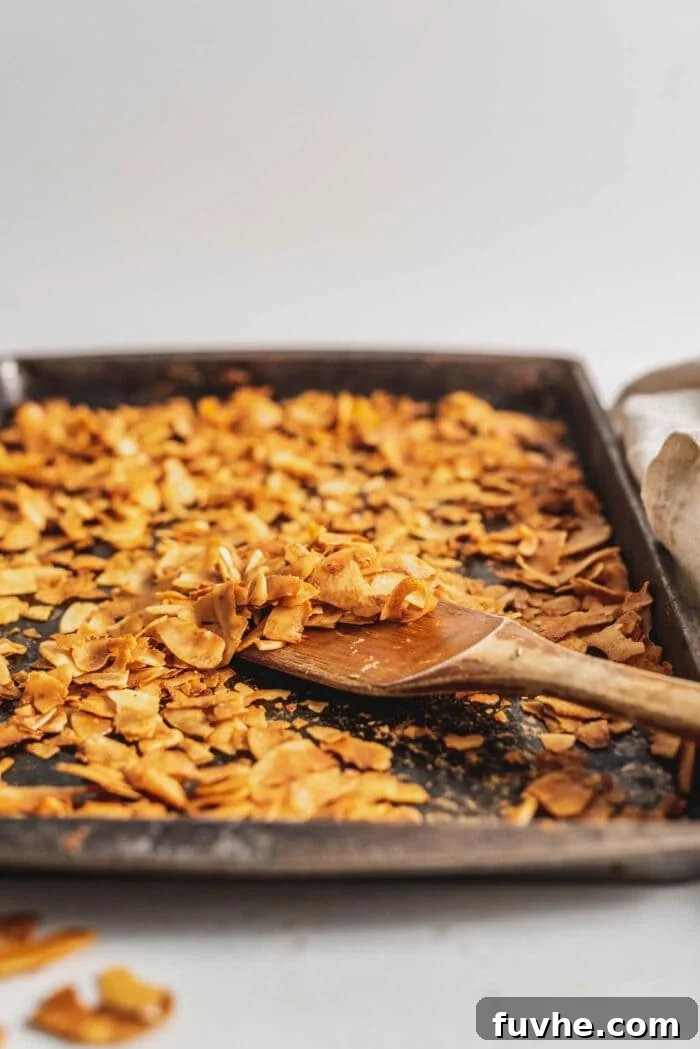 Smoky Coconut Crisps 7 Coconut bacon on a baking try with a wooden spatula.