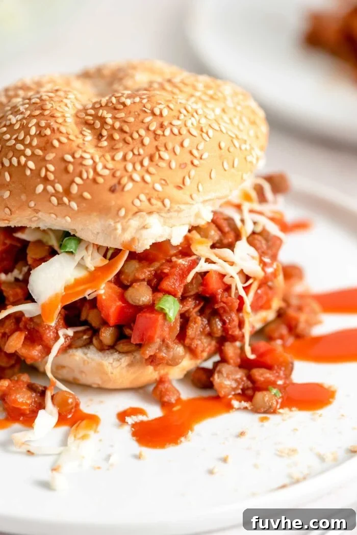 Close up of a lentil vegan sloppy joe sandwich with cabbage slaw on a plate. This image showcases the deliciousness of the plant-based meal, highlighting the rich lentil filling and fresh slaw.
