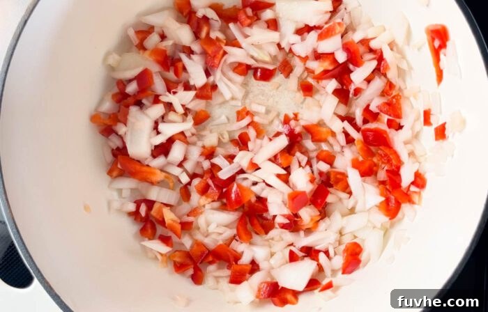 Diced onions and red bell peppers being sautéed in a large pan, softening and releasing their aromas.
