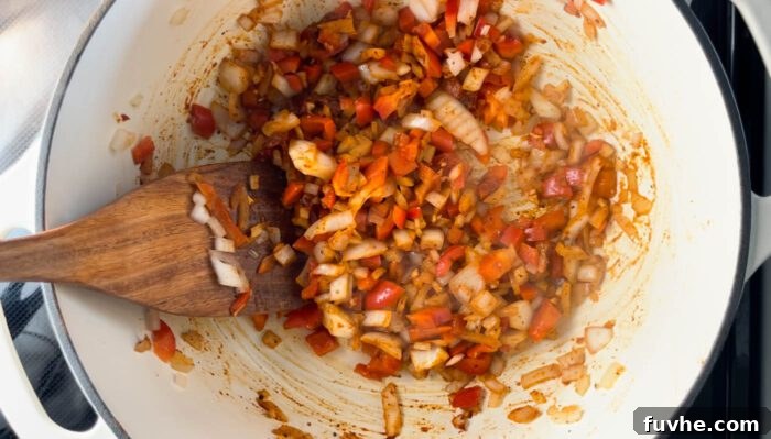 Garlic, chili powder, smoked paprika, and tomato paste being stirred into the sautéed vegetables in a pan, toasting the spices.