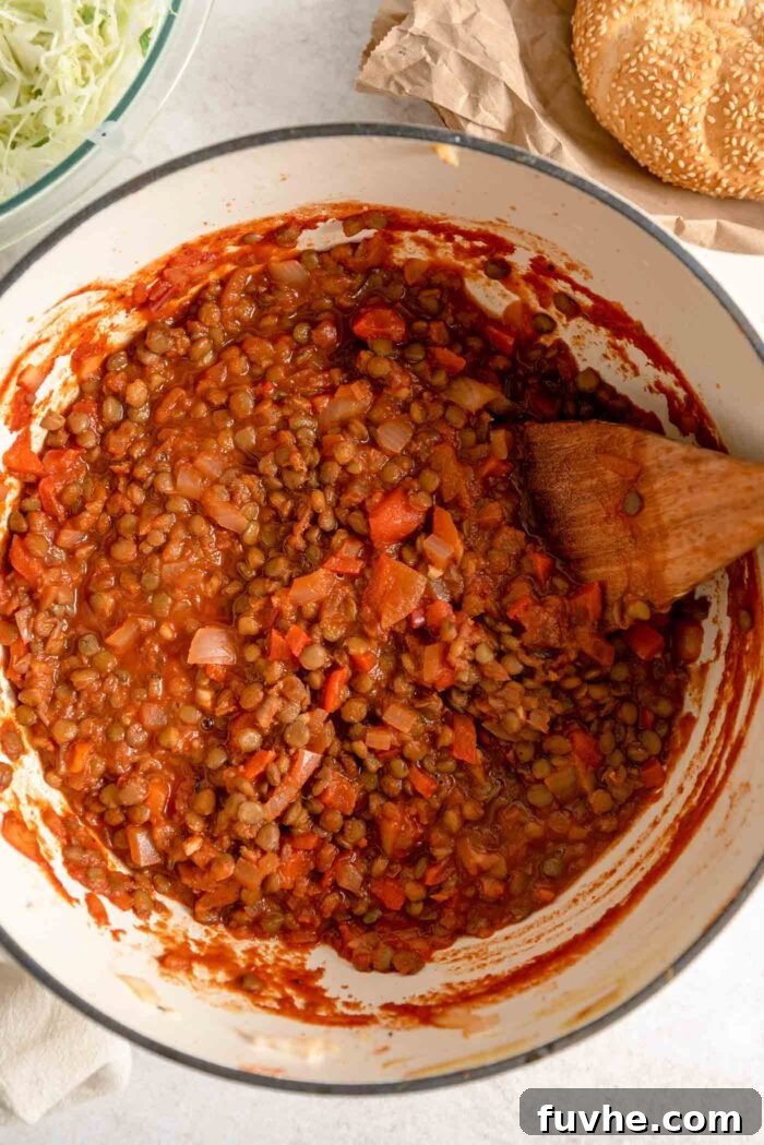 Vegan lentil sloppy joe sauce simmering in a large saucepan with a wooden spoon, showcasing its thick and rich texture.