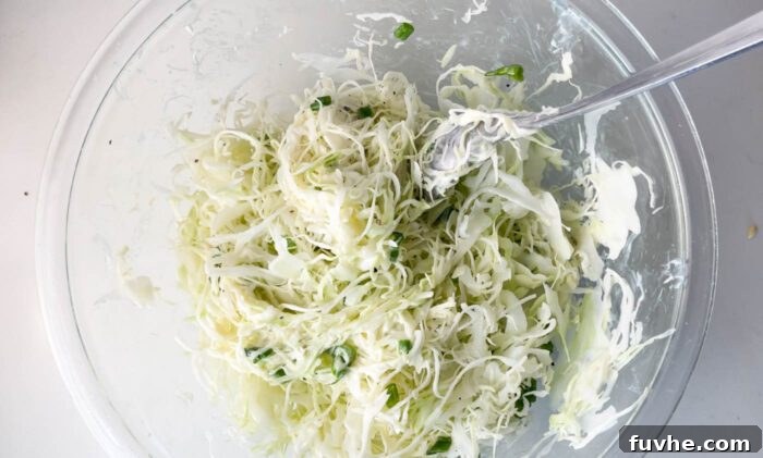 Creamy coleslaw being mixed in a large bowl, combining shredded cabbage, green onions, and a tangy dressing.