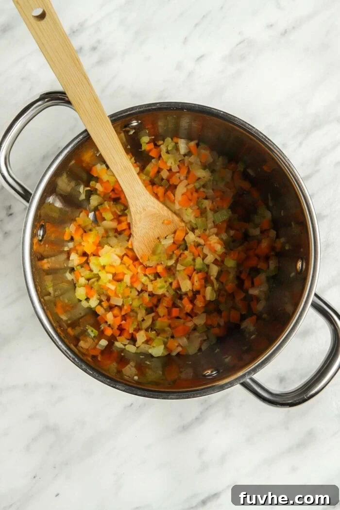 Hearty Plant-Based Minestrone 4 Cooked, chopped carrot, onion, celery and garlic softening in a soup pot with a wooden spoon.