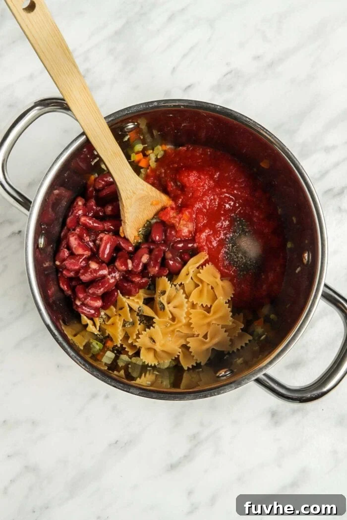 Hearty Plant-Based Minestrone 5 Beans, pasta, and tomato sauce simmering in a large soup pot.