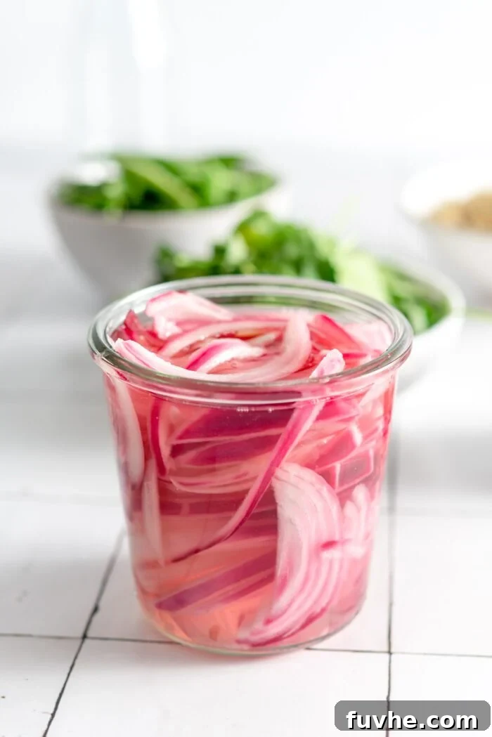 A jar of pickled red onions with two bowls of fresh greens in the background.