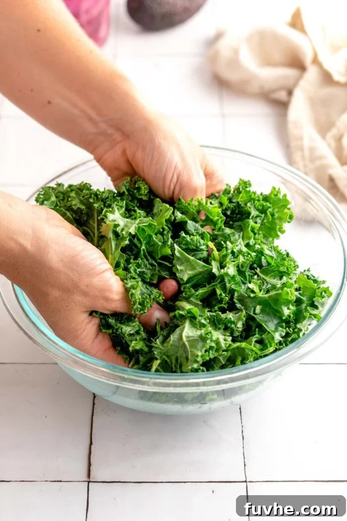 Two hands massaging chopped kale in a glass mixing bowl.