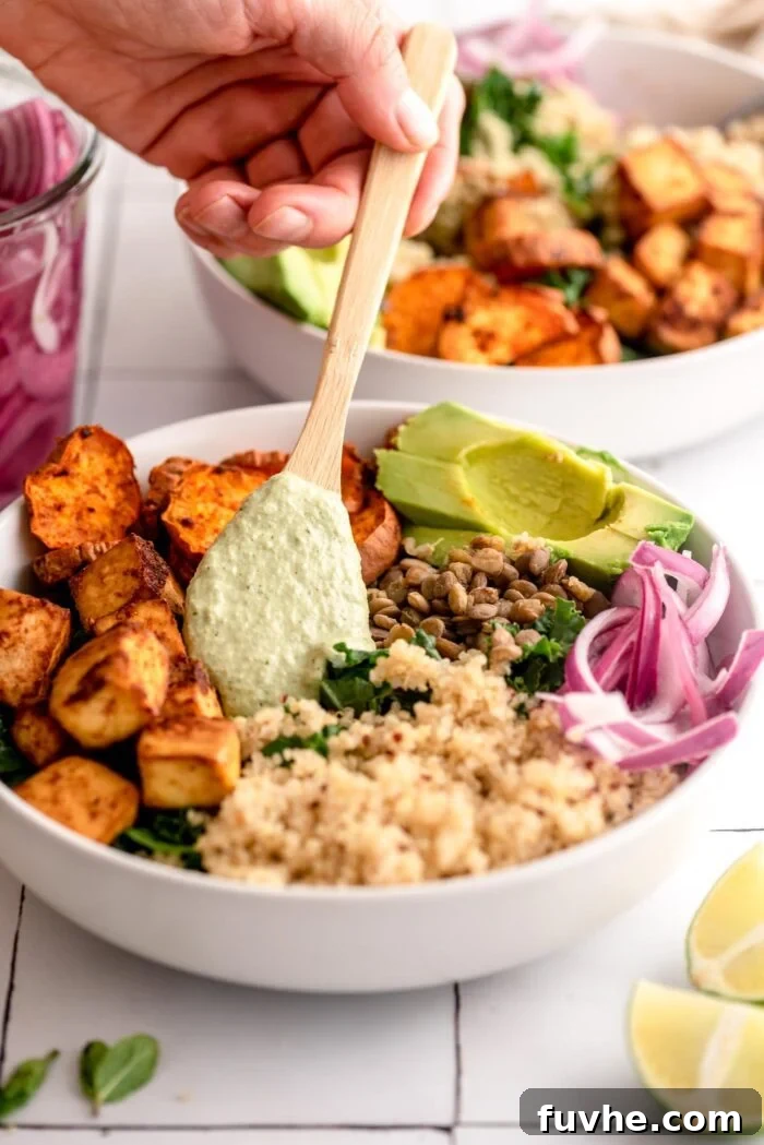 Adding a spoonful of herb hemp dressing to a bowl with quinoa, sweet potato, lentils and tofu.