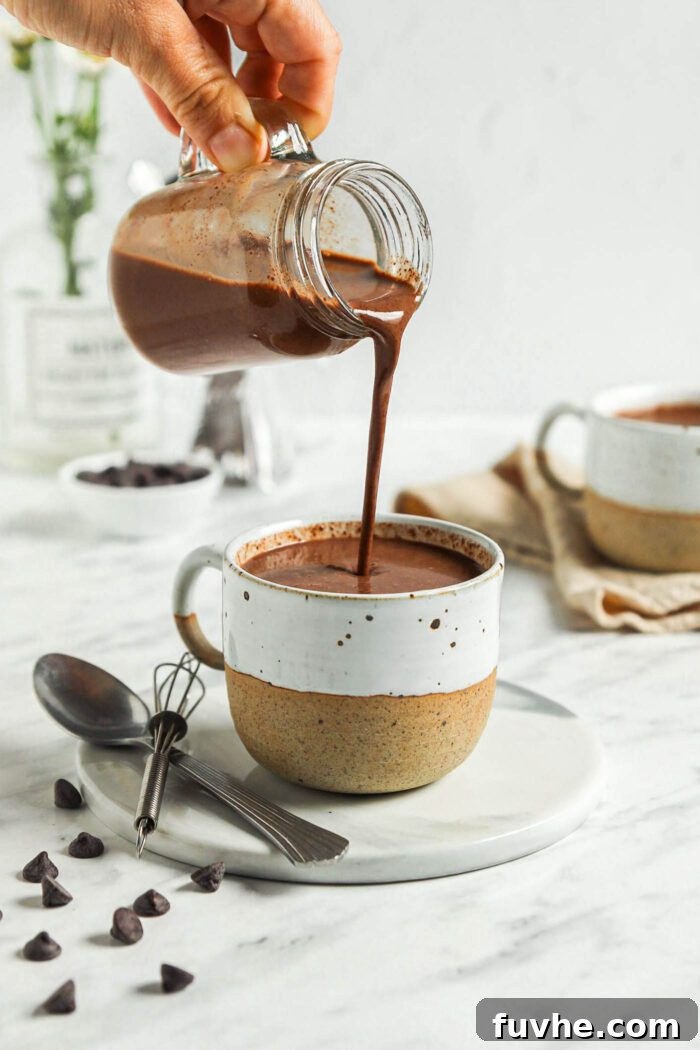 Decadent Plant-Based Hot Chocolate 6 Pouring hot chocolate from a glass jar into a mug.