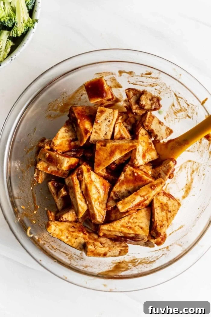 Cubed tofu, freshly cut and glistening, tossed with rich BBQ sauce in a mixing bowl, ready for baking to absorb all the delicious flavors.