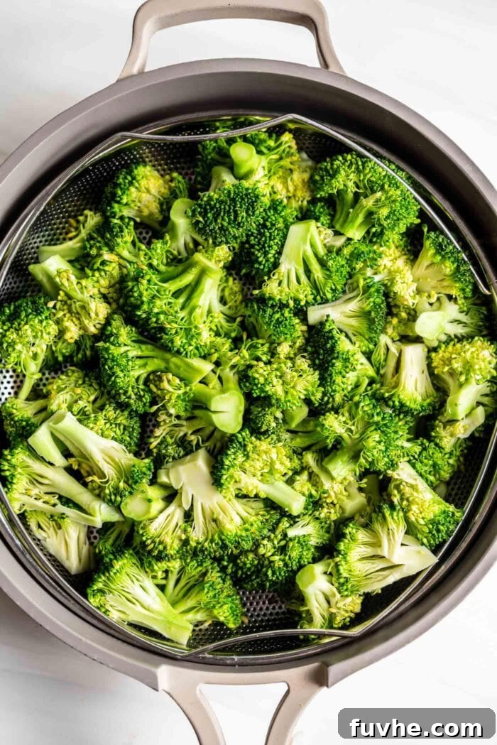 Fresh, bright green broccoli florets neatly arranged in a steamer basket, capturing the steam from a pot below, indicating healthy cooking.