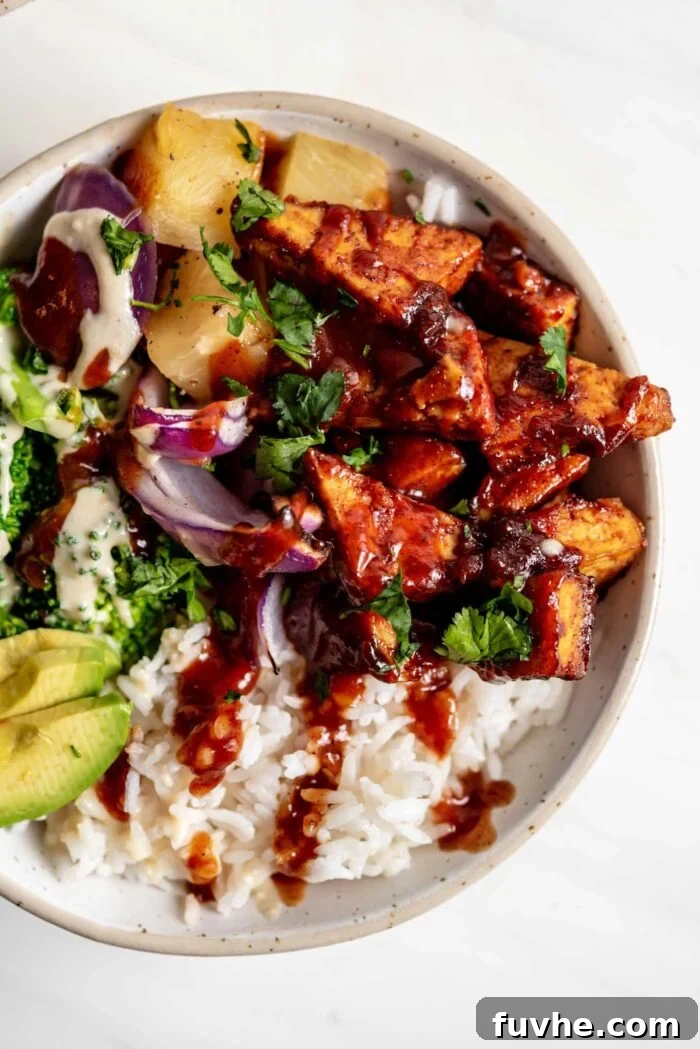 A close-up, overhead view of a vibrantly colored vegan BBQ tofu bowl, generously filled with golden brown rice, saucy BBQ tofu, creamy avocado slices, sweet red onion, and tangy pineapple, showcasing a satisfying and wholesome meal.