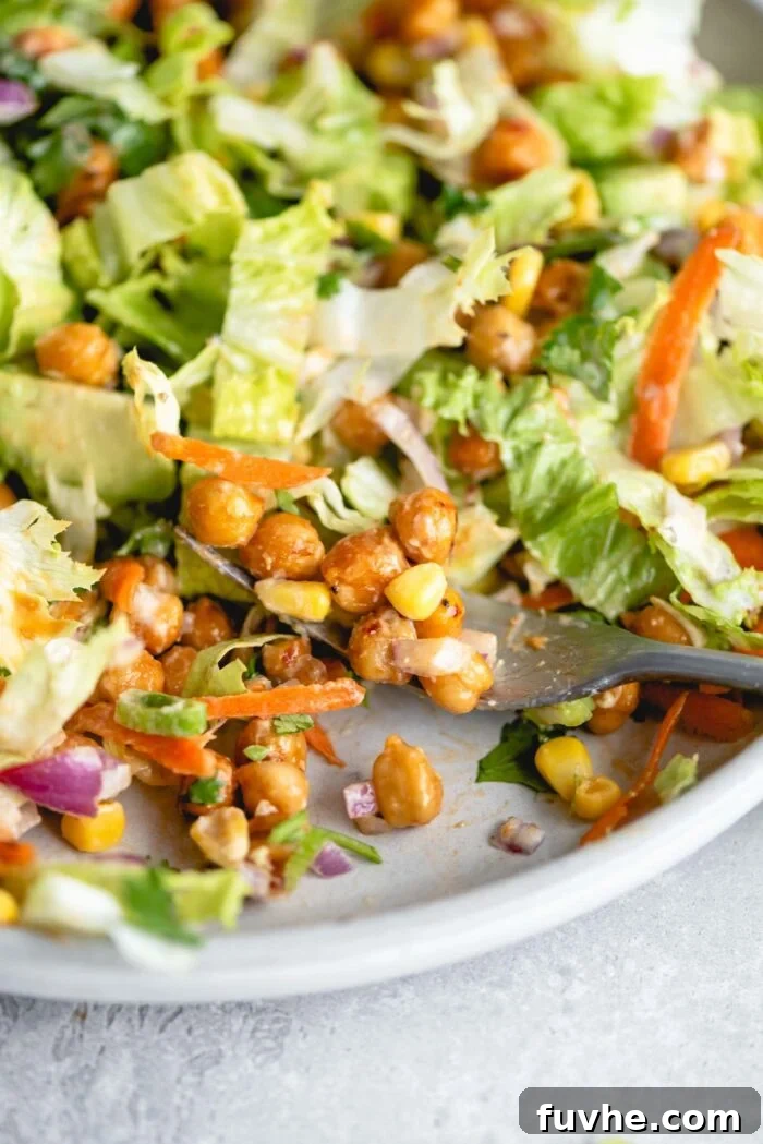 Smoky Vegan BBQ Chickpea Salad 3 Close up of a fork of BBQ chickpea salad with red onion, green onion, lettuce, carrot and corn.