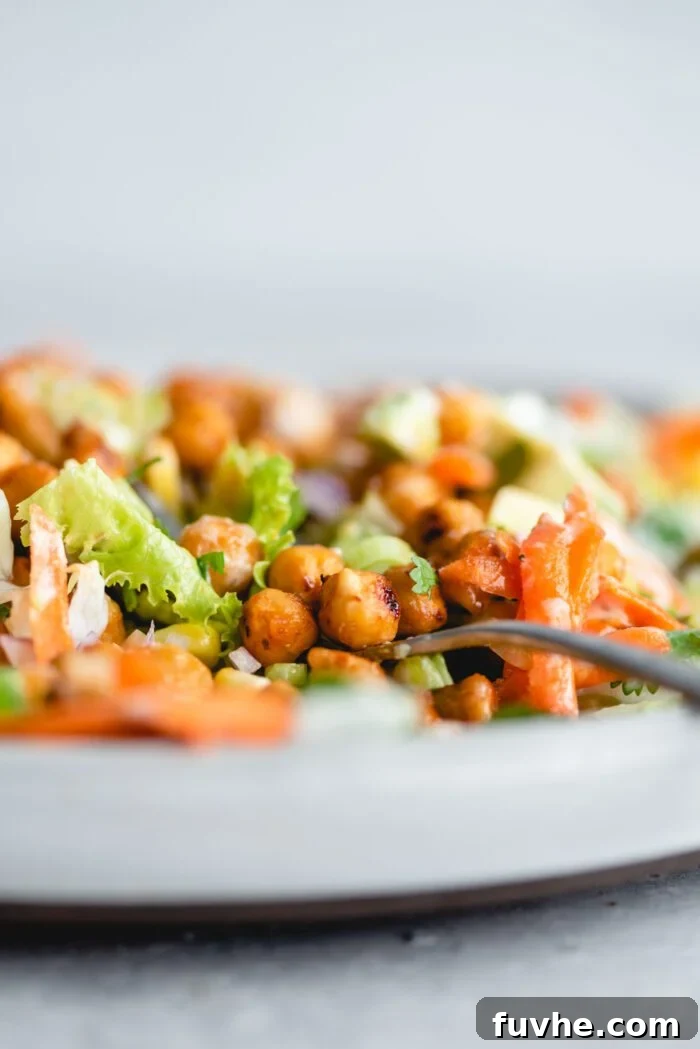 Smoky Vegan BBQ Chickpea Salad 7 Close up of a few BBQ chickpeas sitting on a fork on a plate of BBQ chickpea salad with lettuce, corn and carrot.