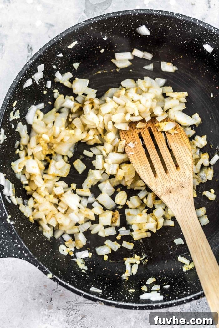 Onions, garlic and ginger with green curry paste being cooked in a skillet.