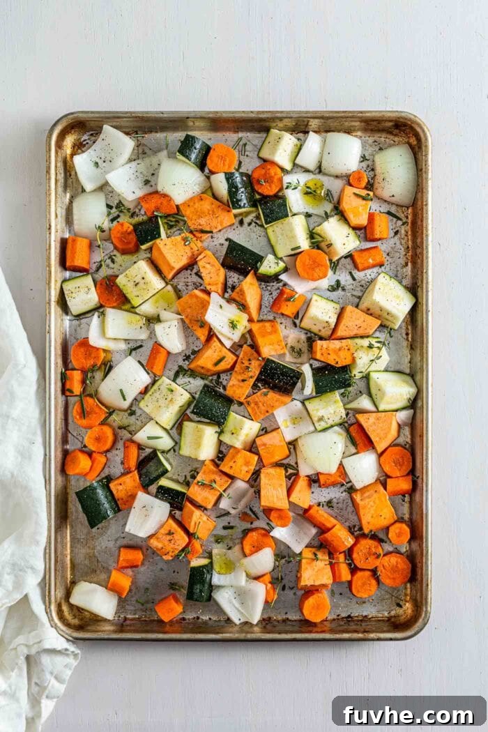 Various chopped root vegetables on a baking tray sprinkled with rosemary and thyme, ready for roasting.