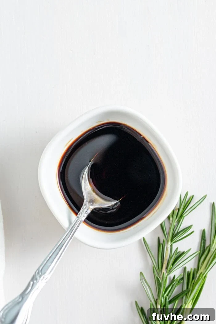 Balsamic dressing in a small dish with a spoon, accompanied by a fresh sprig of rosemary.