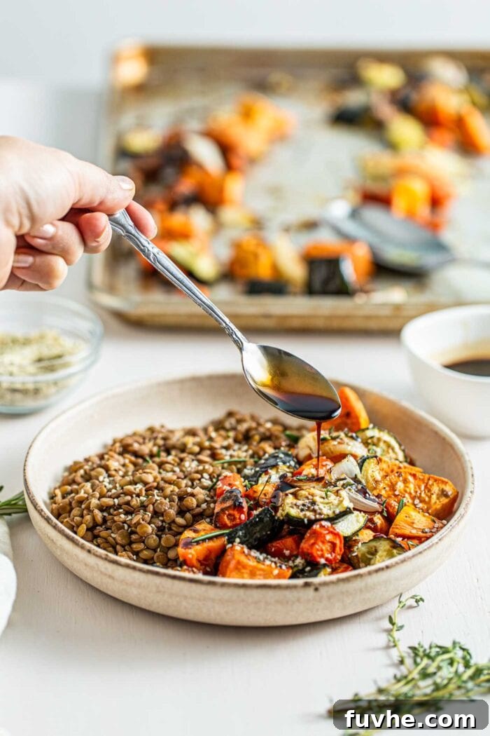 Spooning balsamic sauce over a bowl of cooked lentils and roasted vegetables, ready to serve.