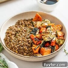 Lentils and roasted vegetables in a bowl. Small dish of balsamic dressing in background.