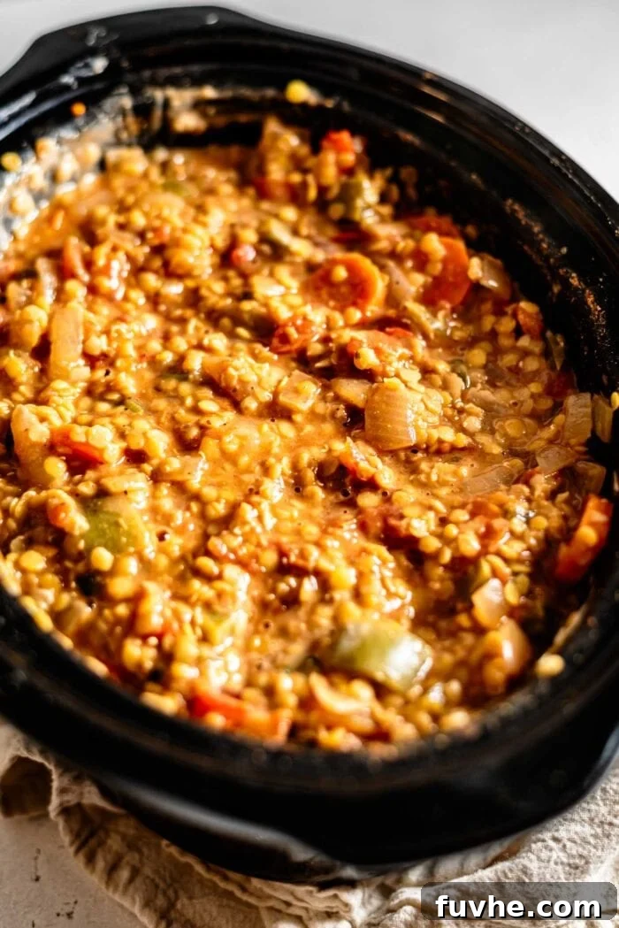 A wide shot of red lentil chili bubbling gently in a slow cooker, its vibrant color and thick texture indicating it's almost ready to serve.