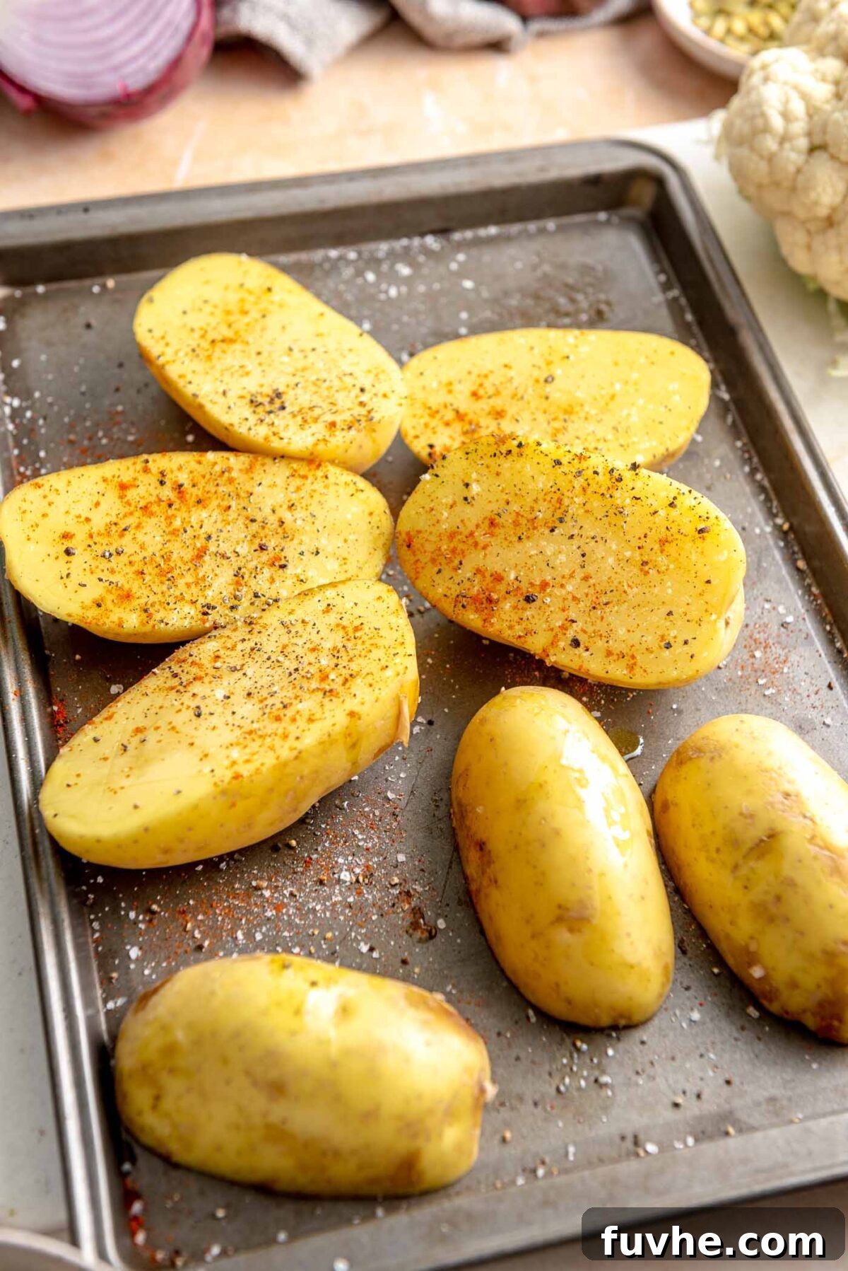 Halved Yukon Gold potatoes seasoned with spices, arranged cut-side down on a baking sheet, ready for roasting.