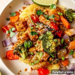Plate of spaghetti squash noodles with peanut sauce, tofu cubes, roasted vegetables, sesame seeds and green onion.