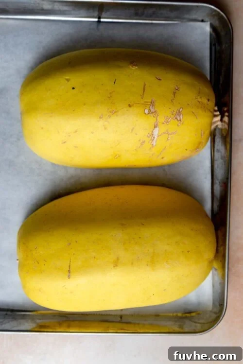 Two halves of a spaghetti squash placed cut side down on a baking sheet.