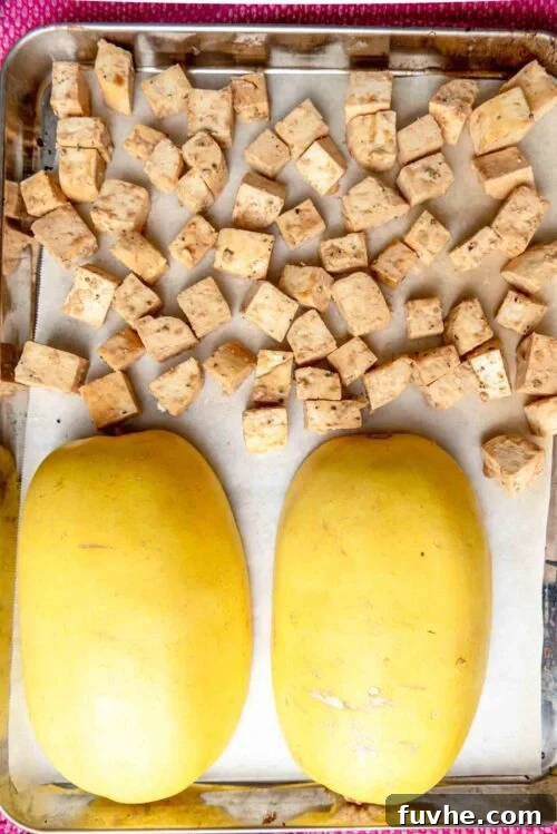 A baking sheet with tofu on one half and two halves of a spaghetti squash on the other.