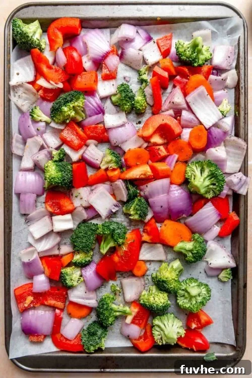 Chopped onion, broccoli, carrot and bell pepper on a baking sheet.