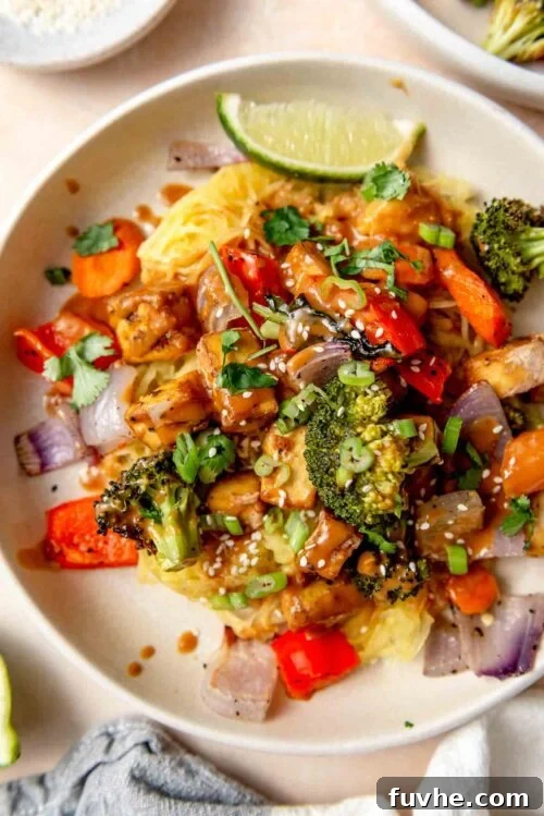 Plate of spaghetti squash noodles with peanut sauce, tofu cubes, roasted vegetables, sesame seeds and green onion.