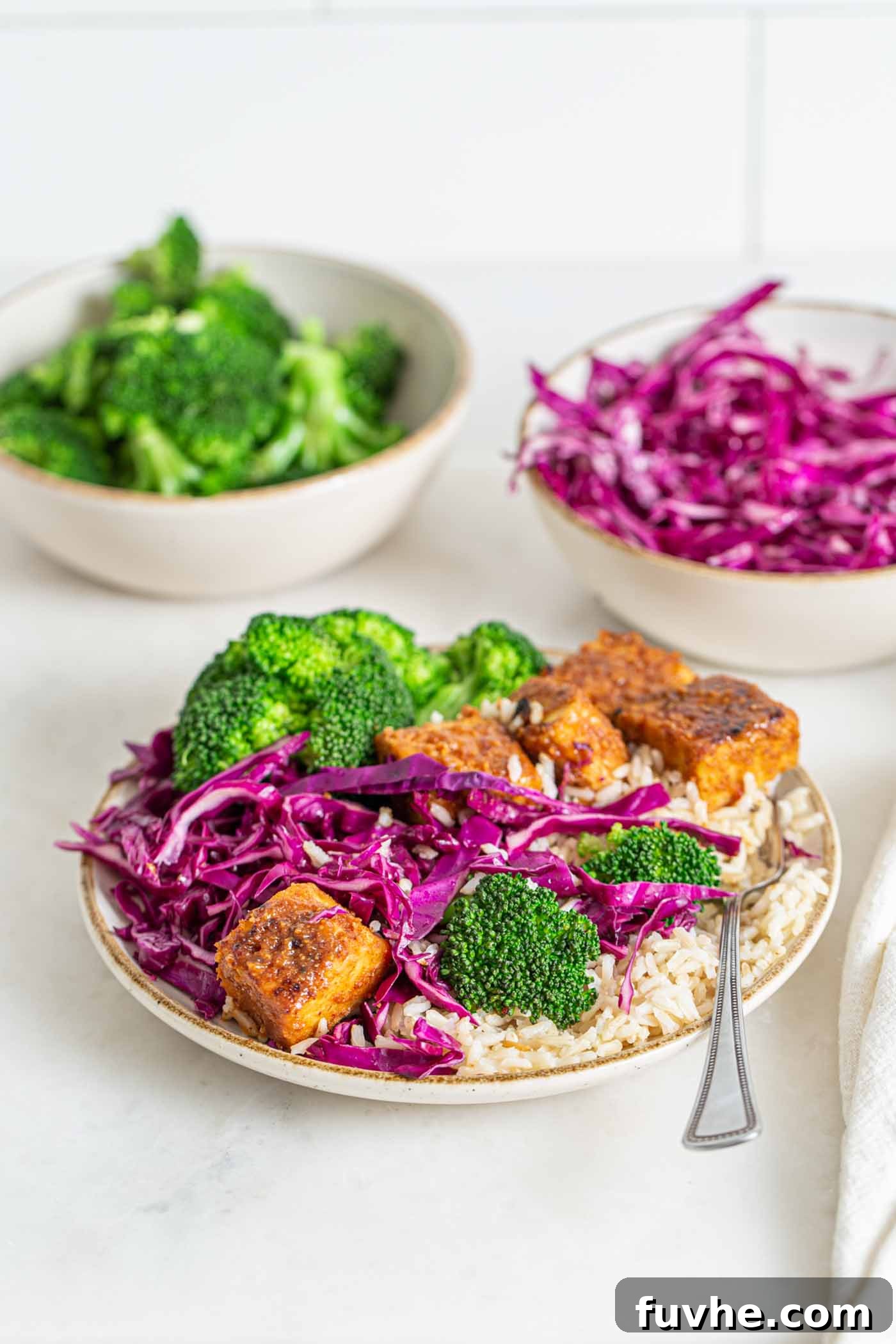 Colourful bowl of brown rice, baked tempeh cubes, broccoli and sliced cabbage.