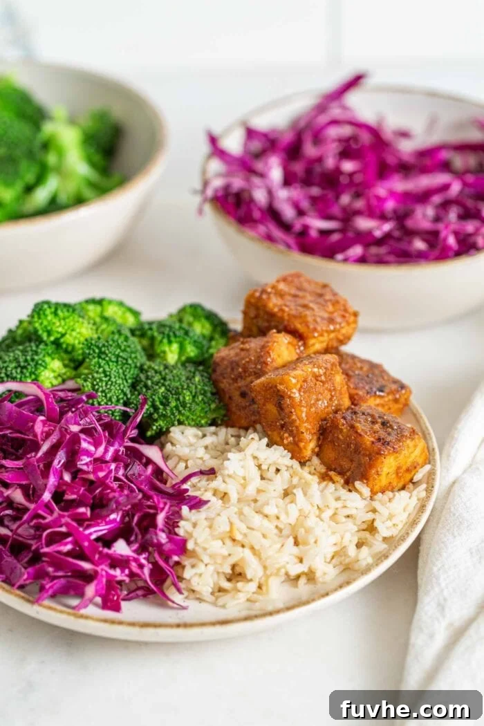 Bowl of brown rice, broccoli, sliced red cabbage and baked tempeh cubes.