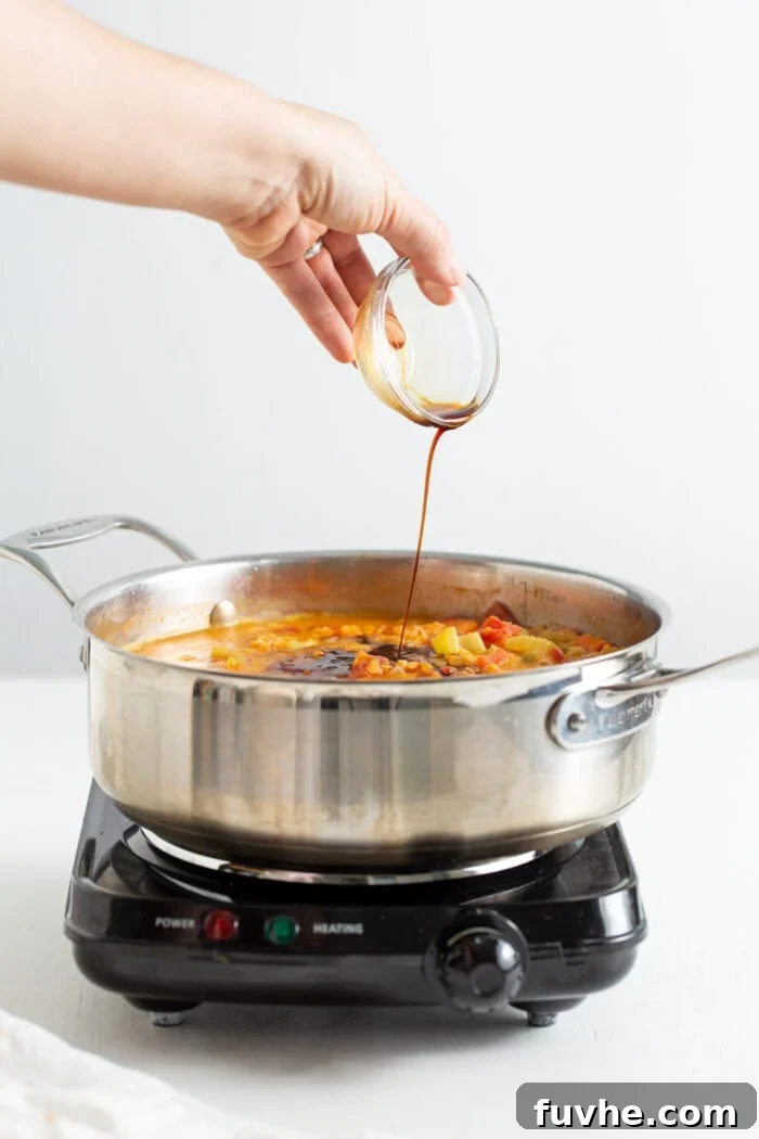 Hearty Curried Lentil Soup 7 A small dish of soy sauce being poured into a pot of simmering lentil soup.
