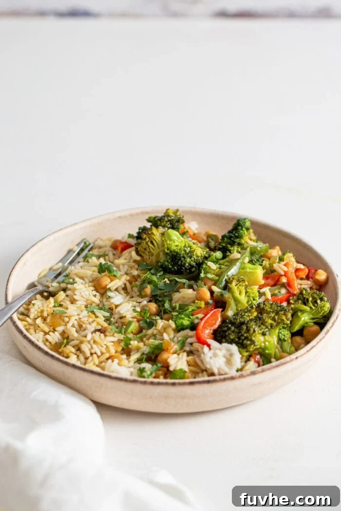 Bowl of rice, vibrant vegetables, and tender chickpeas immersed in a rich, aromatic curry sauce, with a fork resting in the bowl.