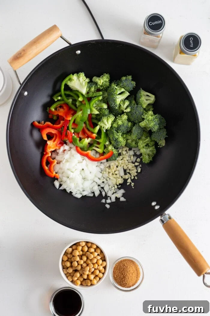 Chopped broccoli, colorful bell peppers, minced garlic, and diced onion are shown together in a wok, ready for cooking.