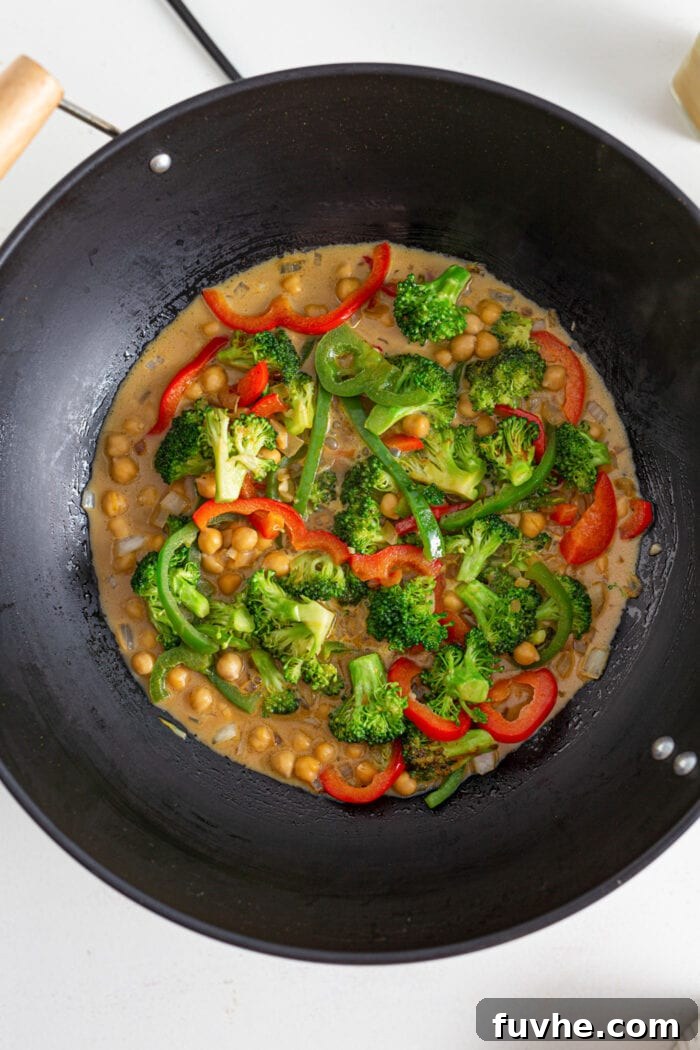 An overhead view captures a bubbling chickpea and vegetable curry in a large wok, showcasing its rich texture and vibrant colors.