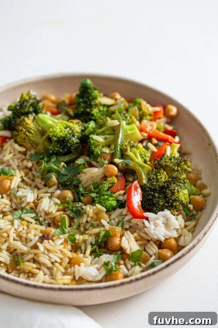 A beautifully plated bowl of rice, overflowing with vibrant vegetables and tender chickpeas in a creamy, flavorful curry sauce.