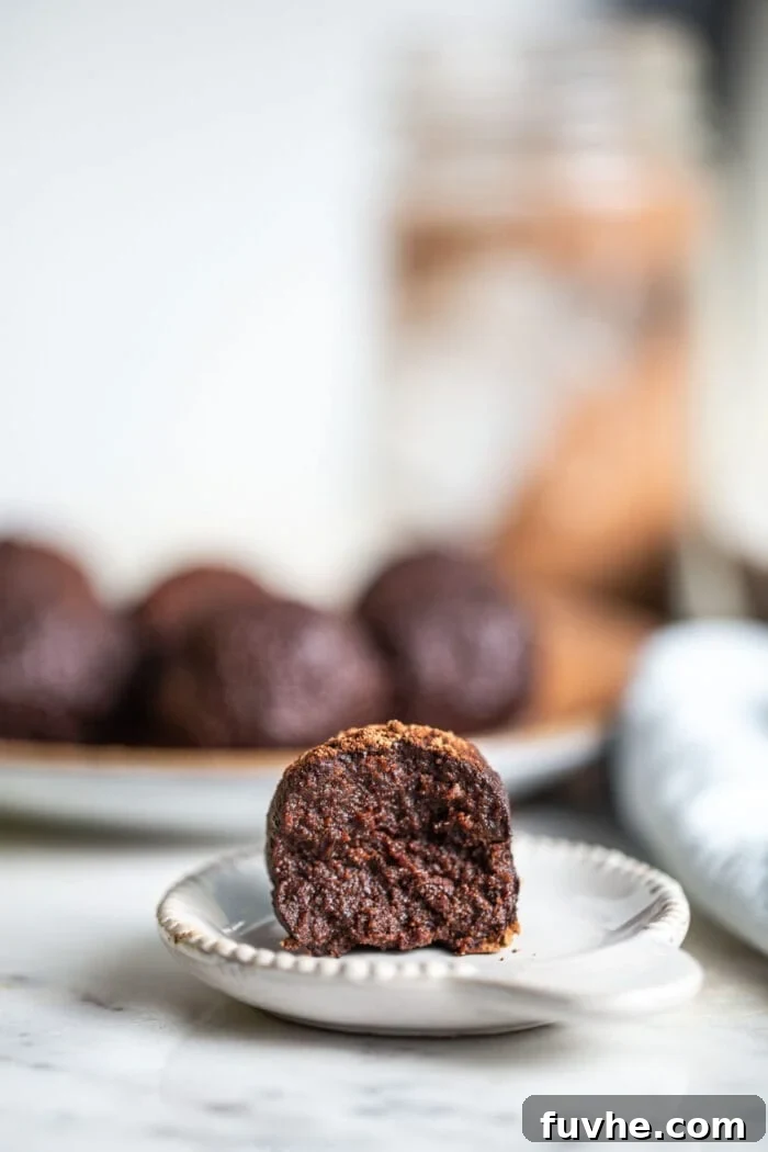 A chocolate tahini date ball with a bite taken out of it sitting on a small white plate.