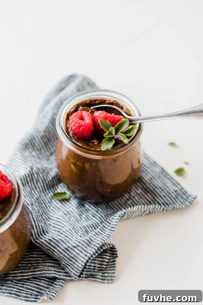 Small glass jar of vegan chocolate avocado pudding topped with raspberries and mint.